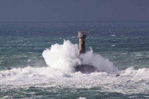 wave crashing over lighthouse in Cornwall